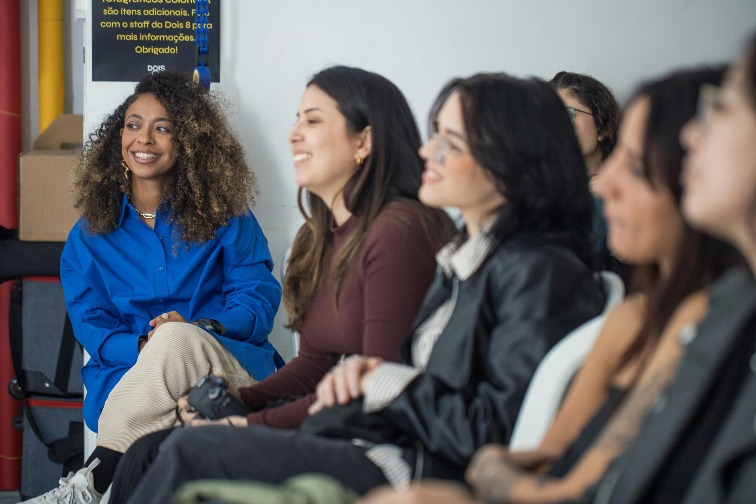 Home A group of diverse women engaged in a casual learning environment, smiling and attentive.