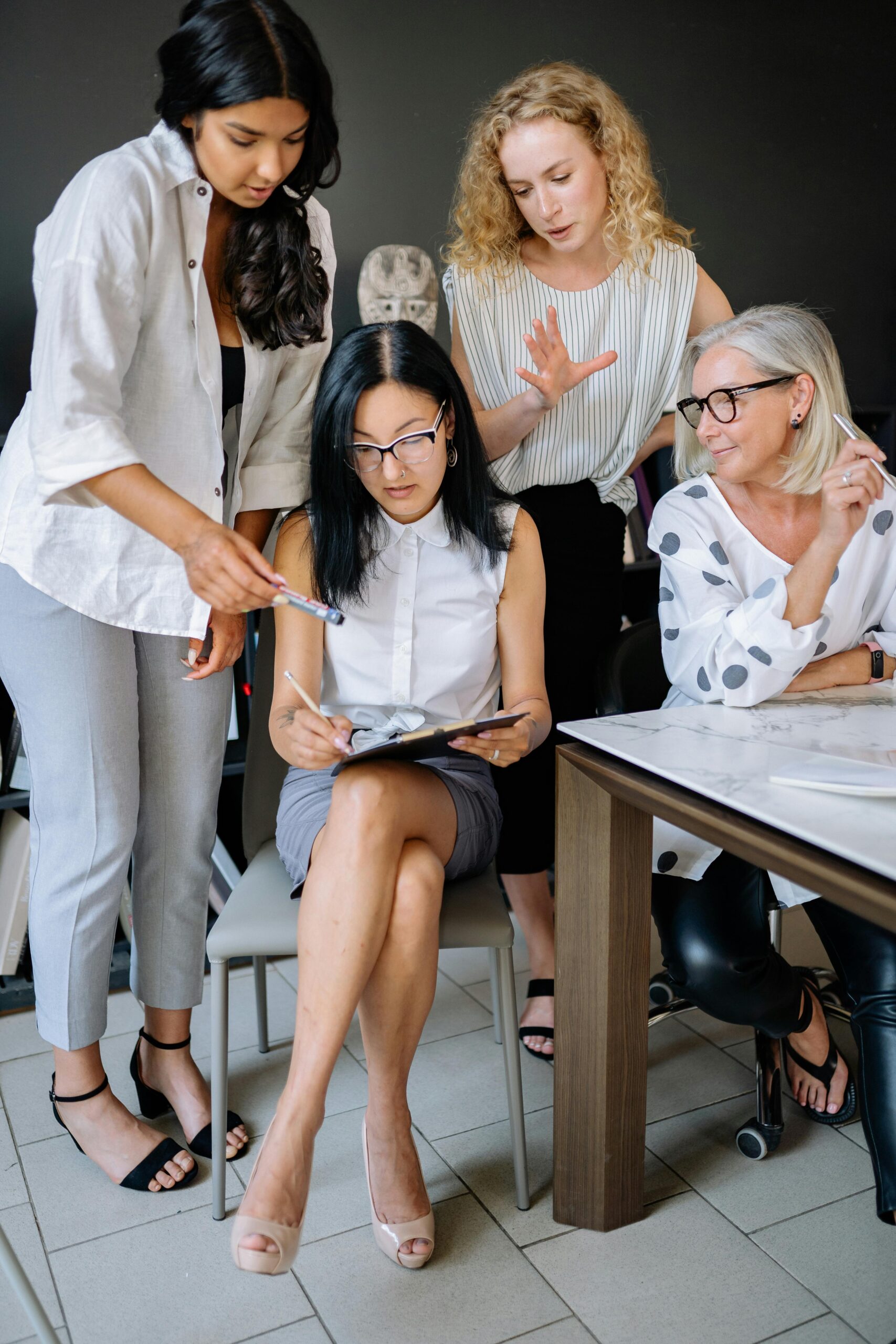 Four diverse women collaborating on a project in an office setting, showcasing teamwork and creativity.